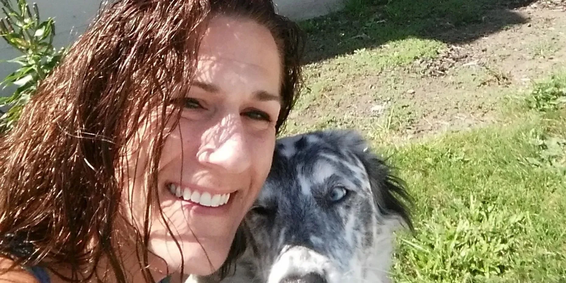 A woman smiling with her dog outdoors on a sunny day.