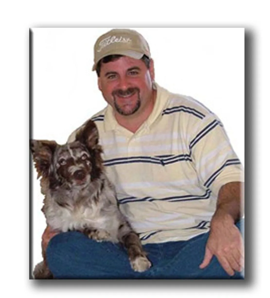 Man in a cap sitting with a brown and white dog.