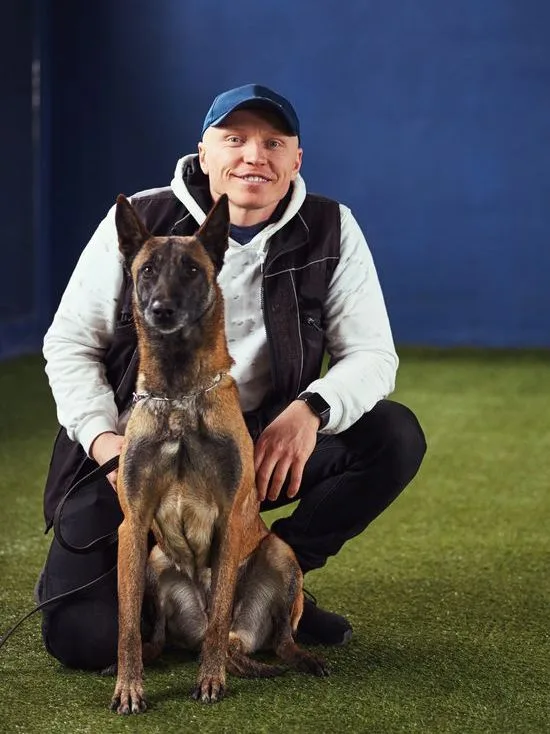 A man is kneeling down next to a dog on the grass.
